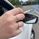 Woman with a smoldering cigarette in her hand hanging it out of a car window. SCDC photograph, July 2024.
